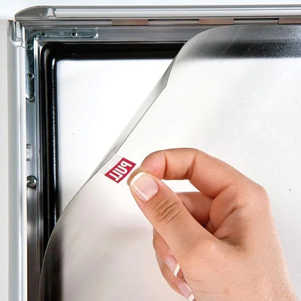 Démonstration d’ouverture d’un cadre clic-clac étanche en aluminium argent. Main soulevant le film de protection transparent avec joint d’étanchéité pour changer l’affiche rapidement. Modèle 100% étanche idéal pour usage extérieur ou milieux humides.