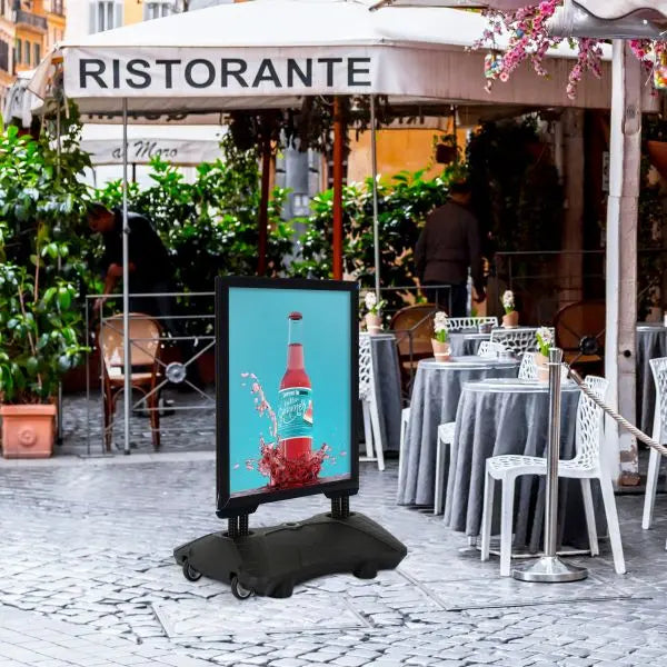 Panneau stop trottoir aluminium noir avec socle lestable installé devant un café